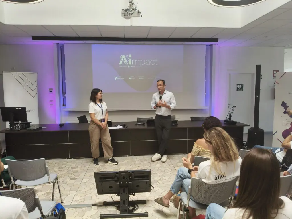 Massimiliano Fedriga interviene durante AI Impact 2026 a Trieste davanti a una platea di partecipanti. Sullo sfondo il logo della manifestazione proiettato sullo schermo principale della sala conferenze