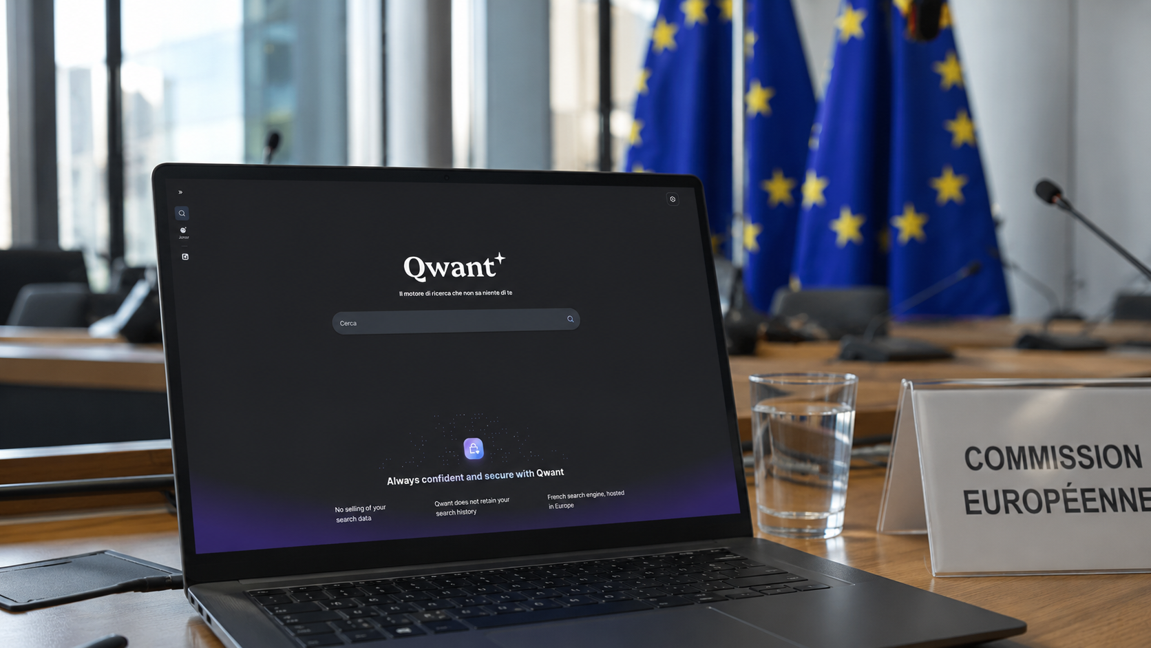 Computer portatile aperto sulla homepage di Qwant in una sala riunioni istituzionale con bandiere dell’Unione Europea sullo sfondo