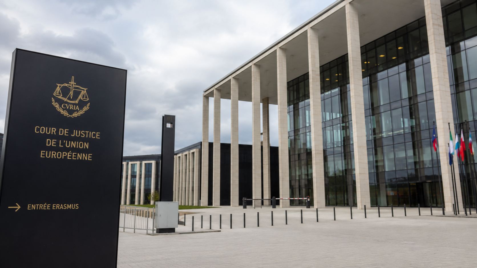 Veduta esterna della Corte di giustizia dell'Unione europea a Lussemburgo, con facciata moderna in vetro e colonne, piazzale d'ingresso e cielo nuvoloso, in stile fotogiornalistico istituzionale.