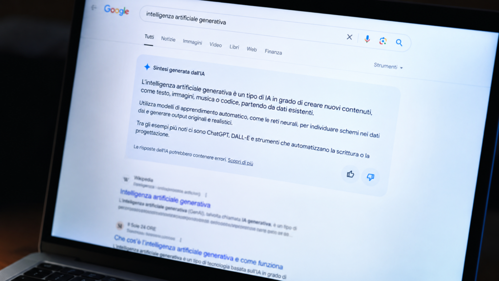Primo piano di uno schermo di laptop che visualizza una pagina di risultati di ricerca con un riquadro di sintesi generata dall'intelligenza artificiale in evidenza sopra un elenco di collegamenti sfocati.