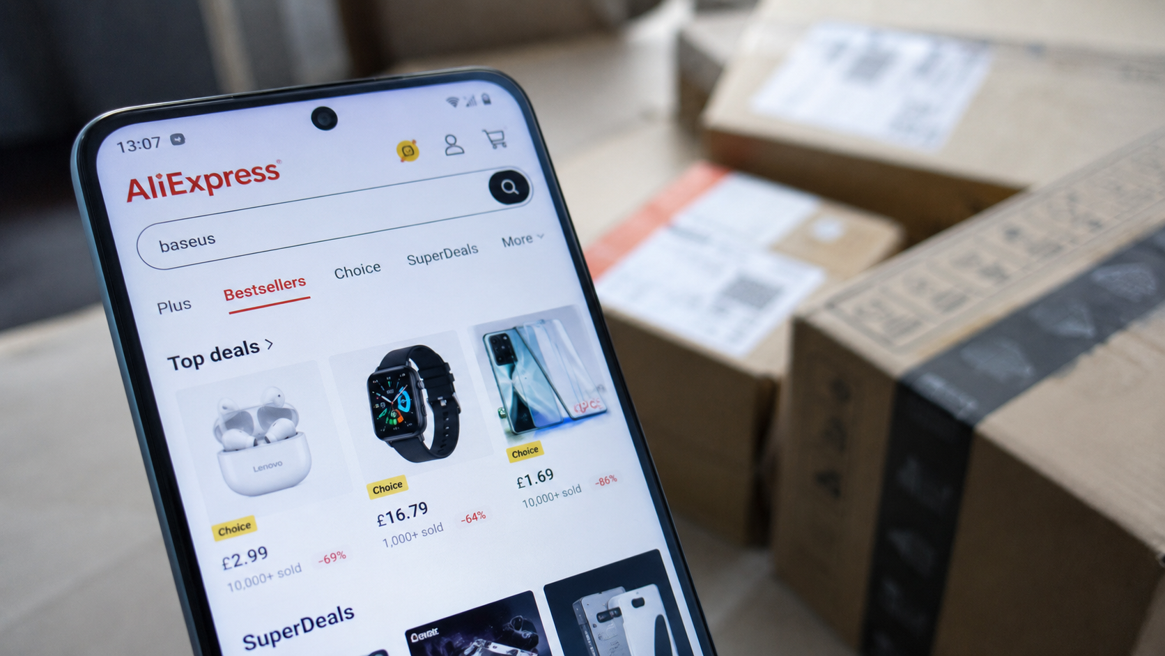 Smartphone con l’app AliExpress aperta per lo shopping online, con pacchi da corriere accatastati sullo sfondo.