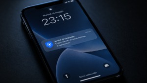 Primo piano di un iPhone appoggiato su una superficie scura, con una notifica di sicurezza visibile sulla schermata di blocco, illuminato da una luce fredda