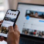 Mani che scorrono il feed di un social network su uno smartphone, con lo schermo di un computer sfocato sullo sfondo e luce naturale morbida.