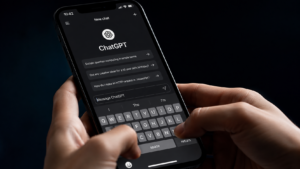 Primo piano di uno smartphone con l’app ChatGPT aperta in modalità scura, mentre una persona digita sulla tastiera. Sfondo scuro e illuminazione da studio, in stile editoriale tecnologico.