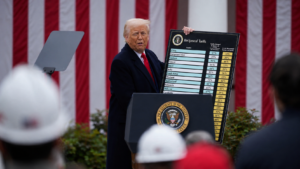 Donald Trump durante un discorso sui dazi reciproci degli Stati Uniti, con la tabella delle tariffe applicate ai principali partner commerciali sullo sfondo della bandiera americana