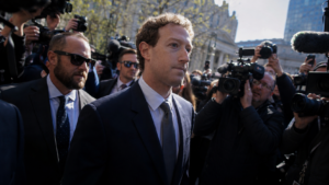Mark Zuckerberg circondato da giornalisti, fotografi e operatori televisivi durante un’uscita pubblica, con telecamere e microfoni puntati verso di lui.