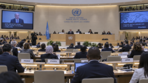 Sala del Consiglio per i diritti umani delle Nazioni Unite durante una sessione, con delegati ai banchi e un relatore che interviene dal podio centrale.