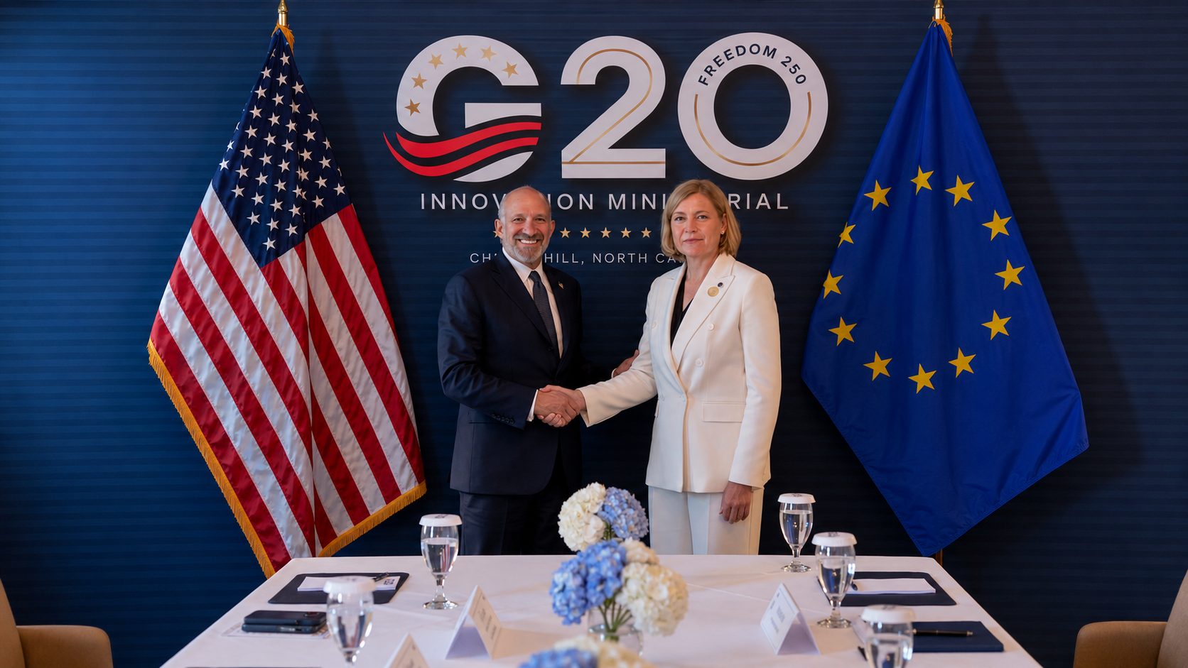 Rappresentanti di Stati Uniti e Unione europea si stringono la mano durante un incontro istituzionale del G20, tra le bandiere USA e UE.