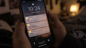 Mani giovani stringono uno smartphone con notifiche Snapchat visibili sullo schermo, in un ambiente domestico in penombra.