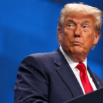 Donald Trump ripreso di tre quarti davanti ai microfoni, con abito blu e cravatta rossa, su sfondo blu. Immagine rielaborata con IA, con etichetta “AI” in basso a sinistra