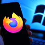 Smartphone con logo Mozilla Firefox in primo piano e schermo di computer con logo Microsoft Windows sullo sfondo, in un ambiente tecnologico illuminato da luce blu.