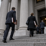 Ingresso di un tribunale federale americano con imponenti colonne in pietra e professionisti in abiti formali che salgono le scale portando documenti.